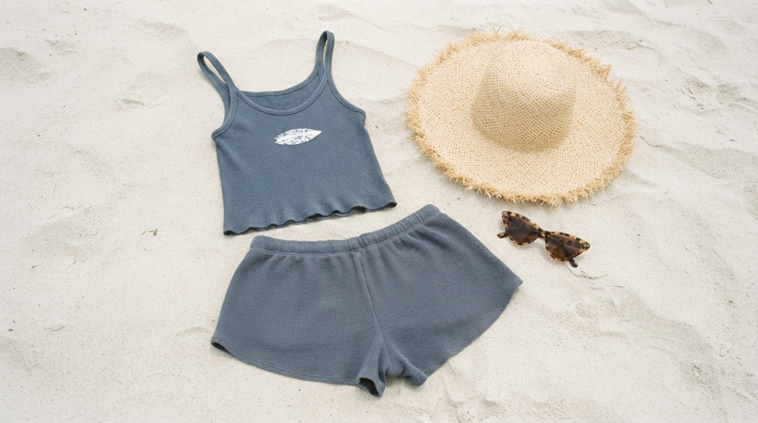 A Curvite vest and surf shorts set laid flat on sand beside a straw hat