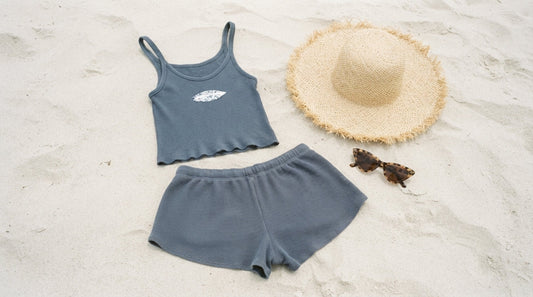 A Curvite vest and surf shorts set laid flat on sand beside a straw hat